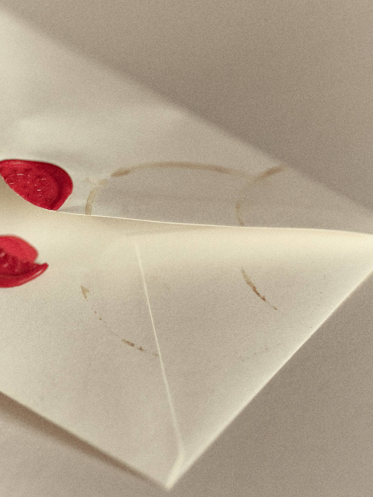 A cream envelope cropped close in soft daylight, two red wax seals at the edge of the frame and faint ring stains left on the paper.