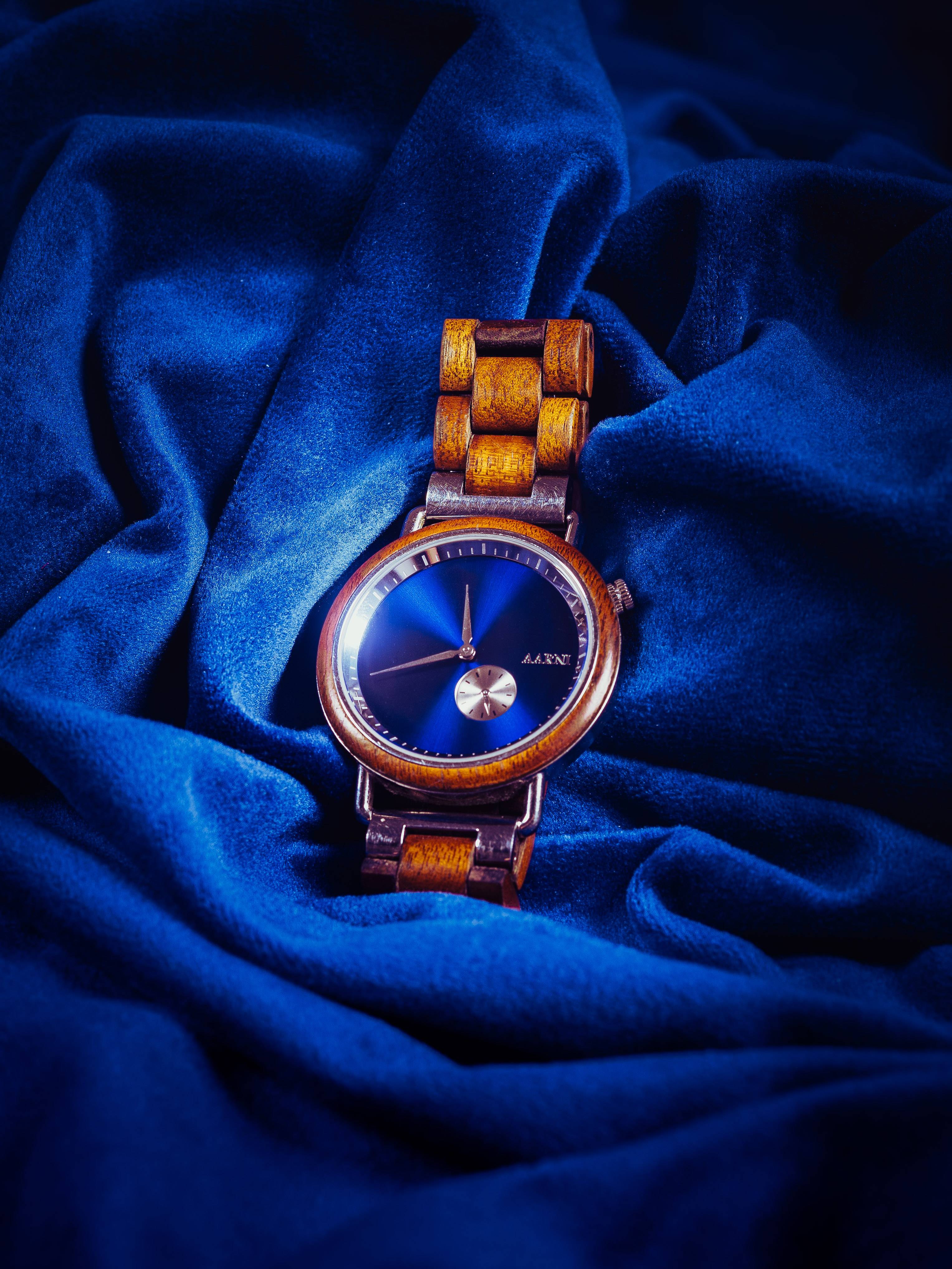 A wooden wristwatch with a deep blue sunburst dial nested in folds of blue velvet, a single highlight raking across the glass.