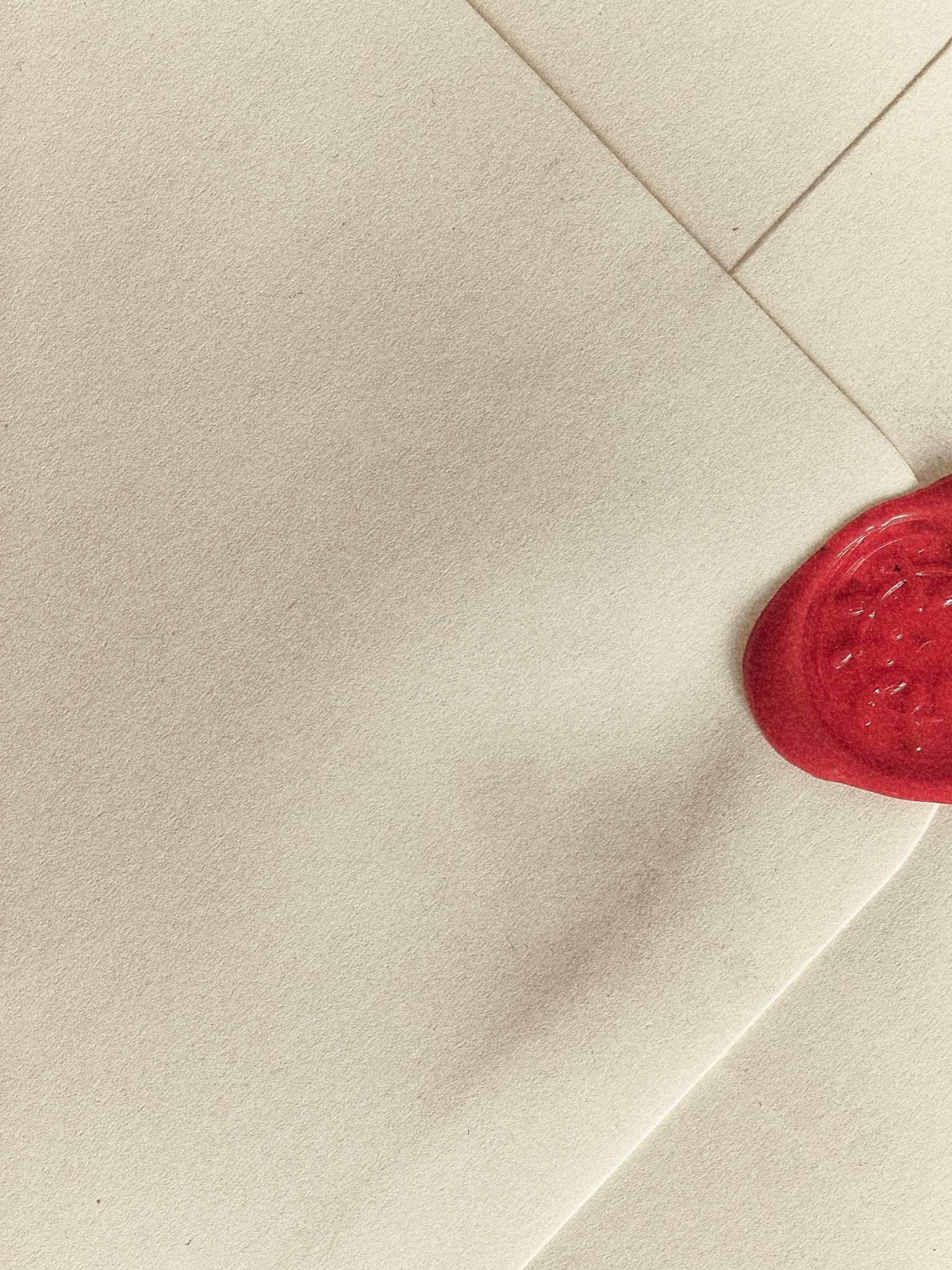 A corner of cream envelope paper in soft light, a red wax seal pressed at the right edge of the frame.
