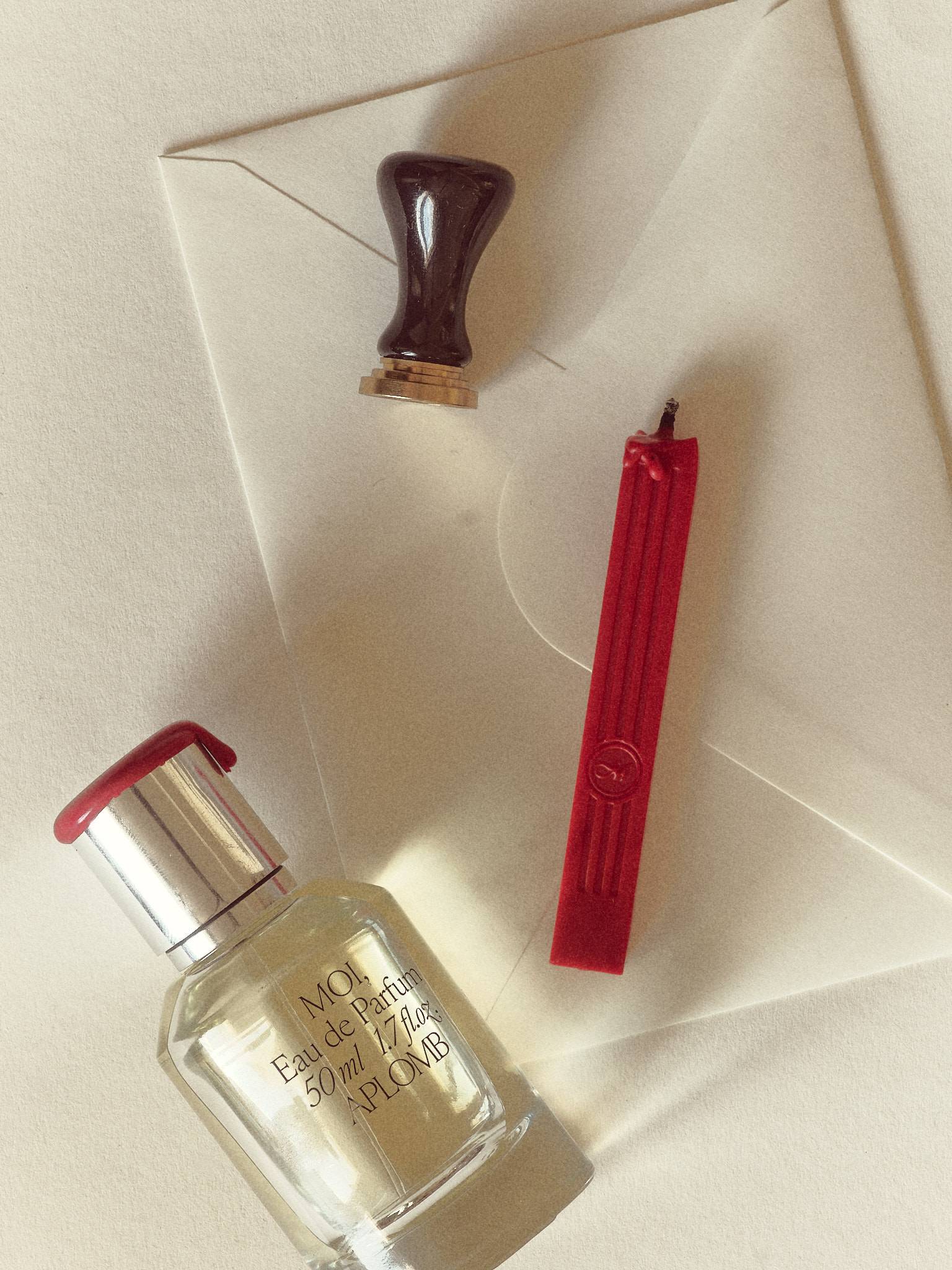 A perfume bottle, a stick of red sealing wax and a wooden-handled seal laid across a cream envelope in soft daylight.